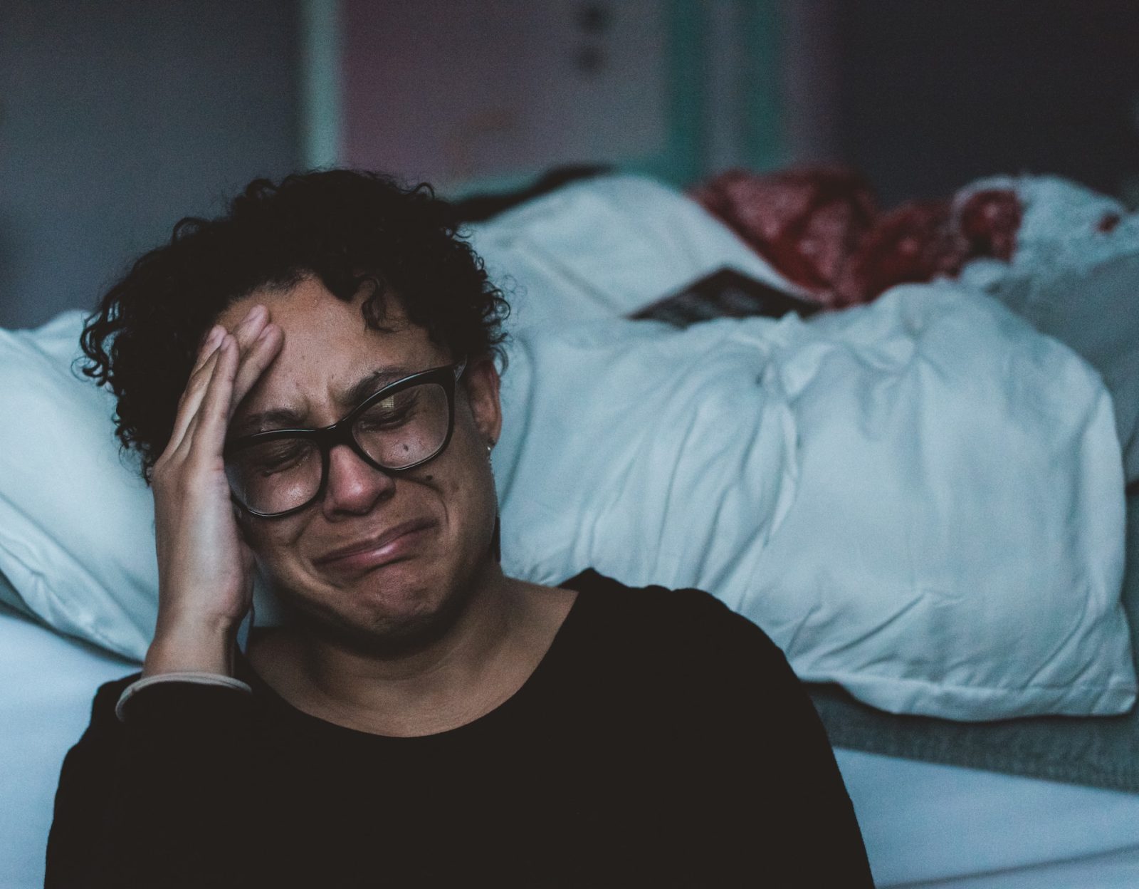 Schwarze Frau mit Brille weint vor Bett