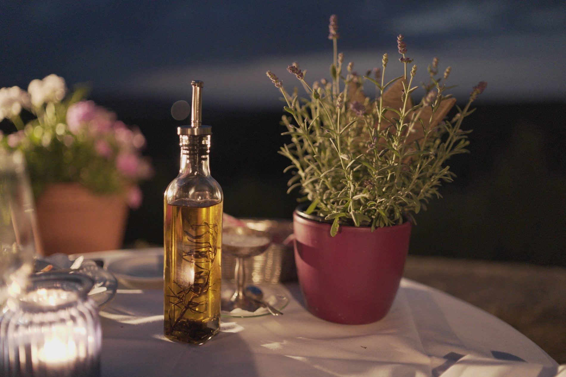 Eine Flasche Öl steht neben einem Topf mit Kräutern auf einem gedeckten Tisch